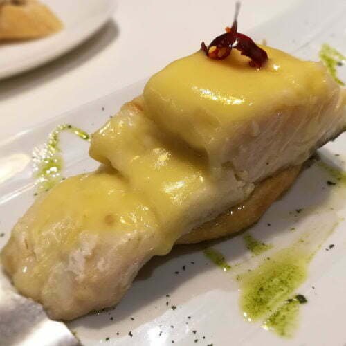 Bacalao al Pil Pil, served on a white plate with a small pattern of mojo sauce on the plate. 