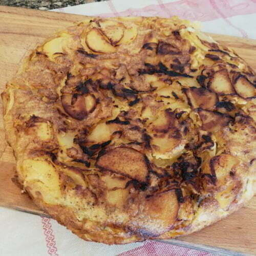 A handmade Spanish tortilla rests on a wooden chopping board in a kitchen setting