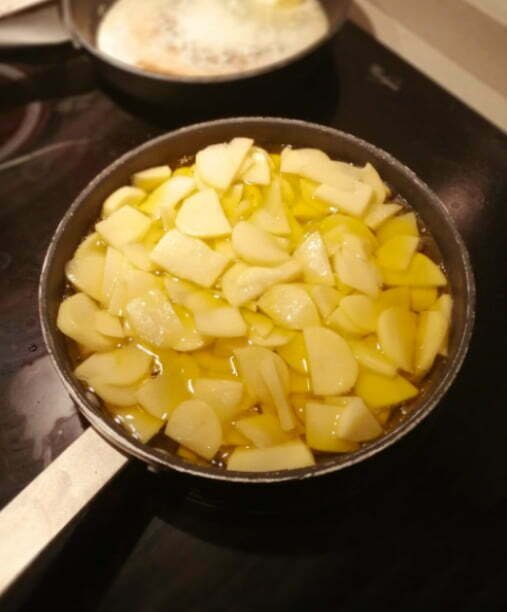 Potatoes cooking in olive oil in a large black frying pan. Kitchen setting