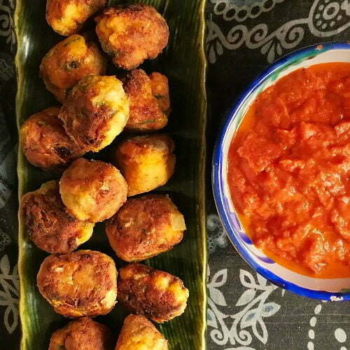 a long green plate of croquetas sits beside a small white bowl of salsa