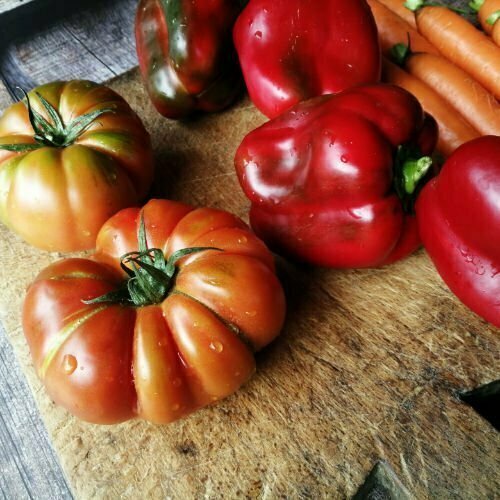 Fresh tomatoes and red peppers sit on a rustic chopping board All ingreients are part of the Mediterranean diet