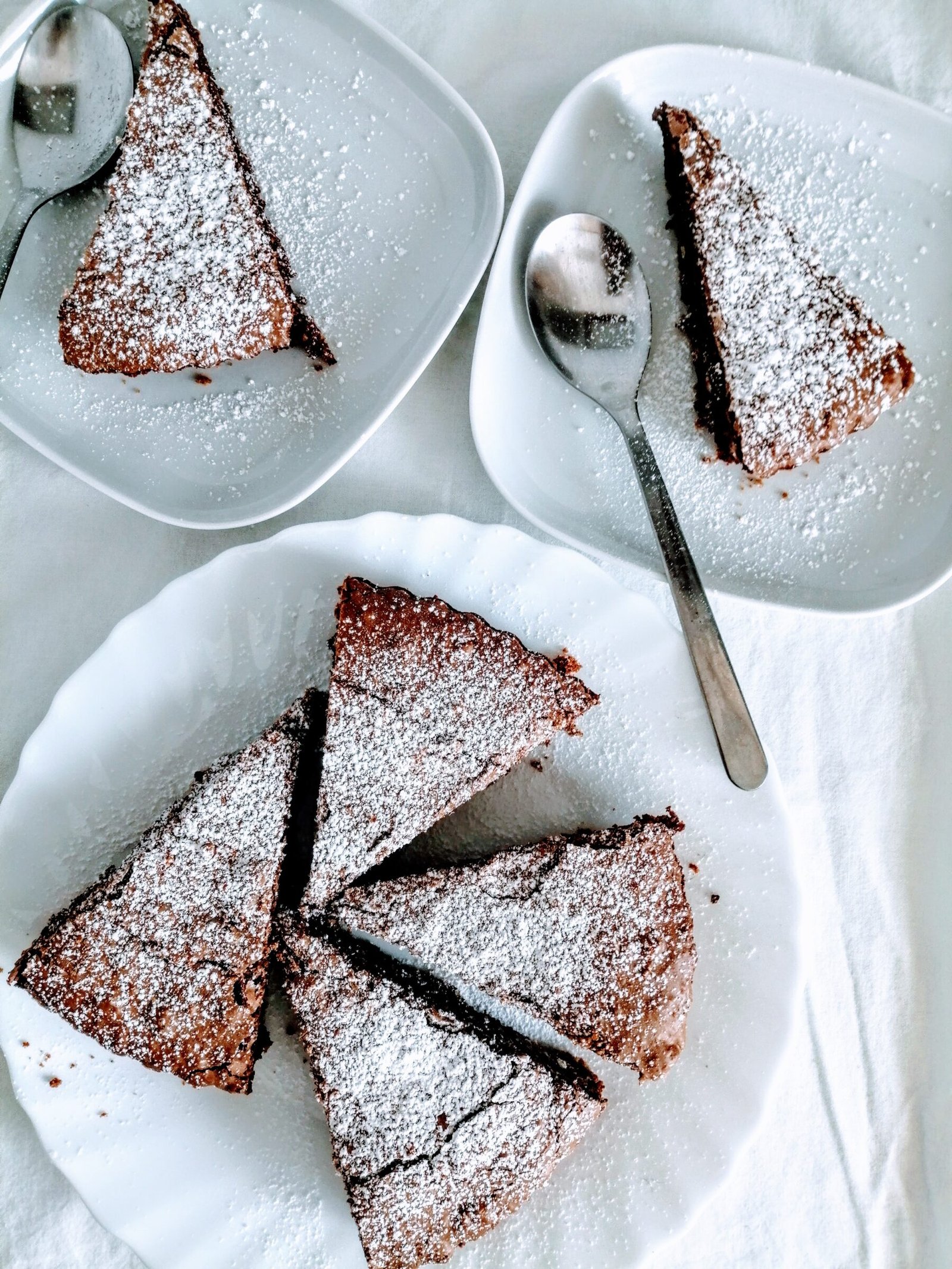 slices of chocolate hazelnut tart sit on a few white plates waiting to be served