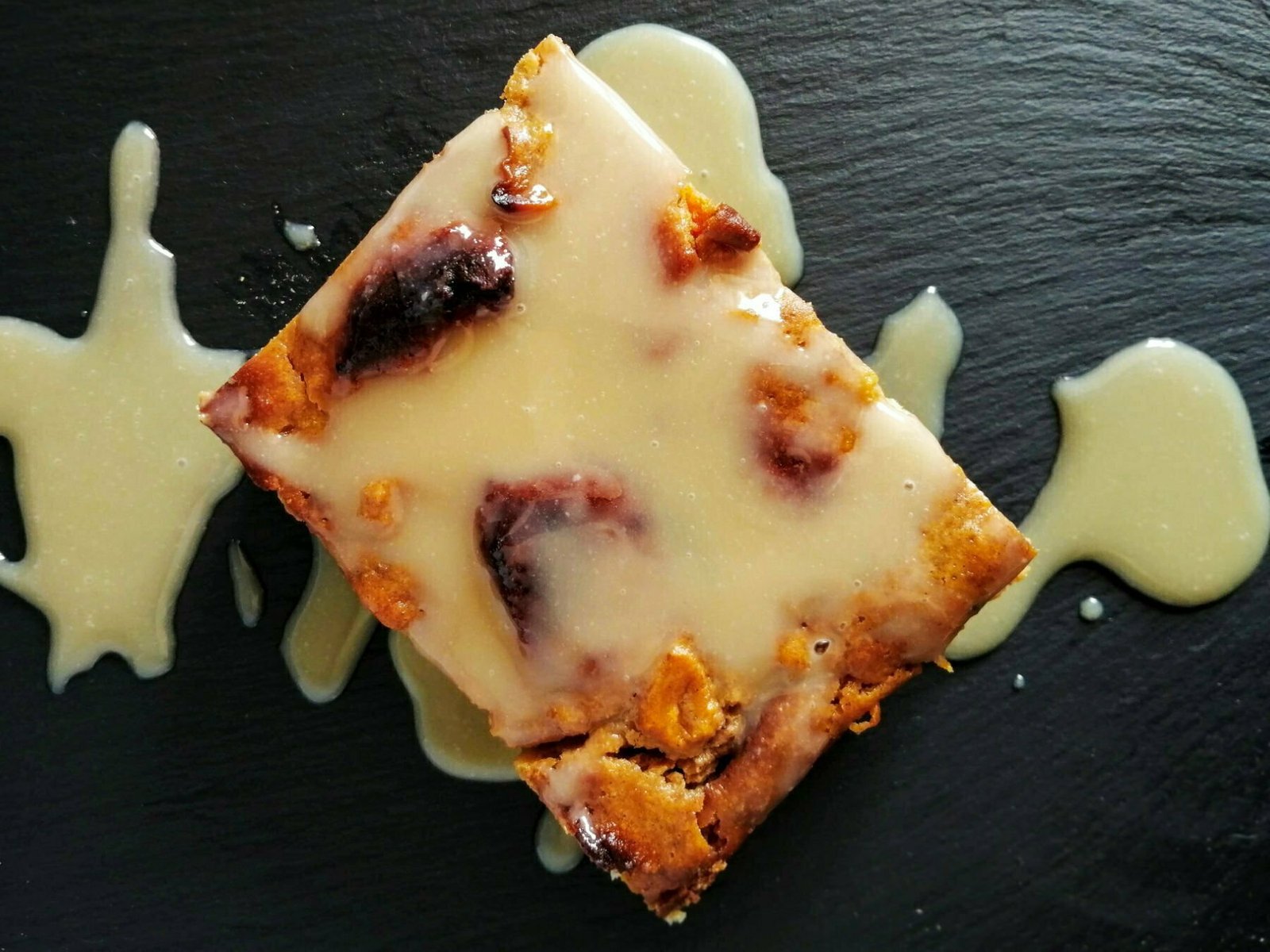 Pumpkin bread pudding sits on a slate plate with a gooey caramel sauce drizzled on top