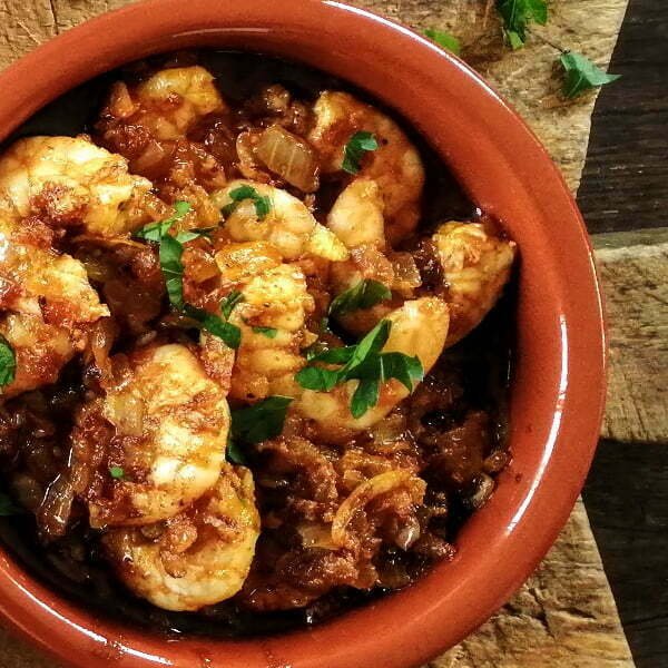 A dish of gambas al ajillo sits on a chopping board