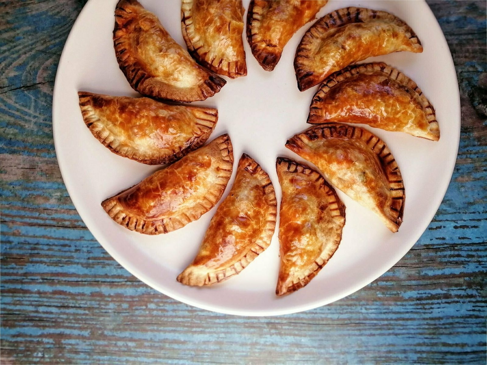 chicken with cider infused chorizo empanadas sits on a white plate on top of a blue wooden benchtop