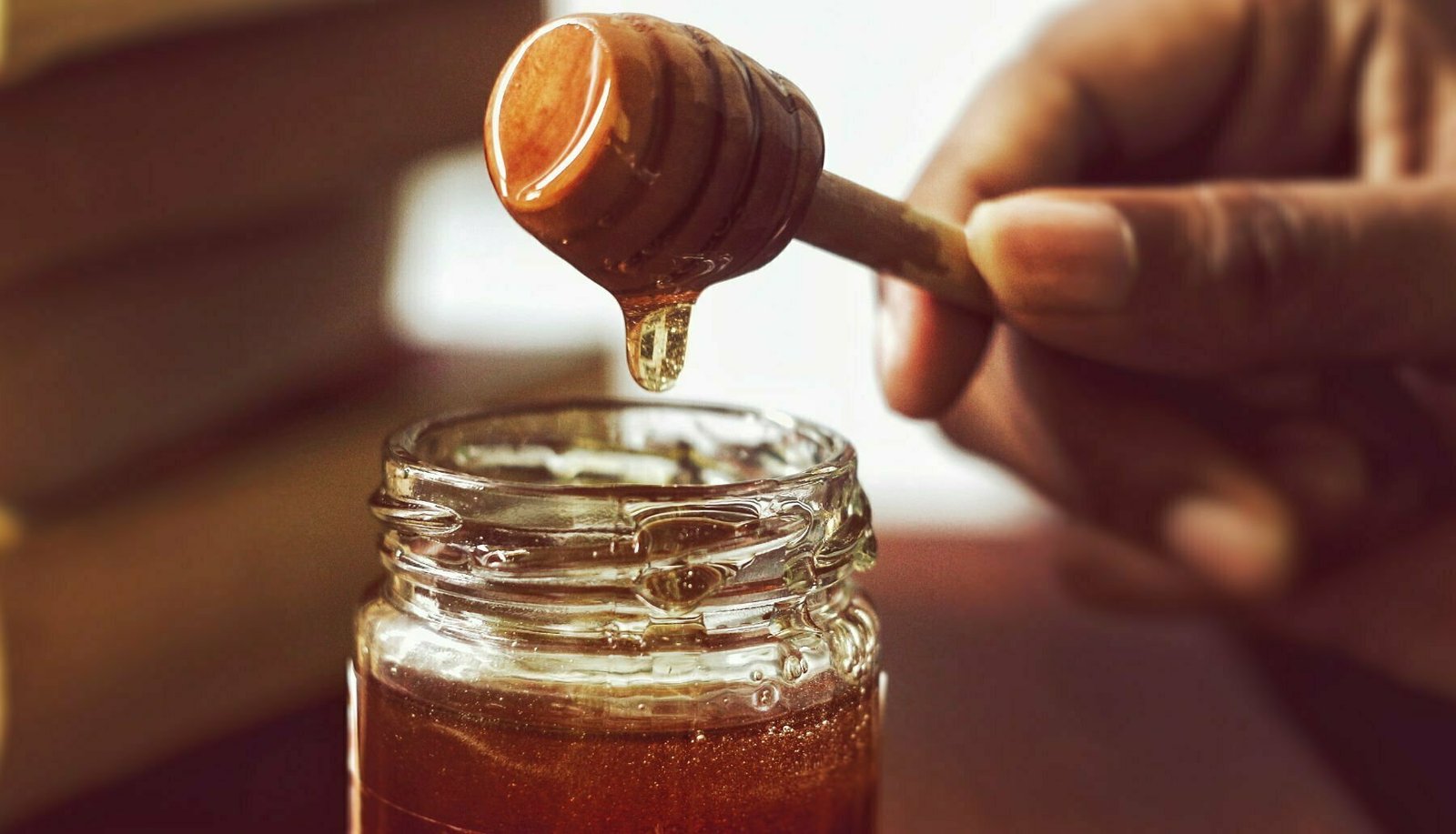 A person with a honey ladel removes some honey from a jar