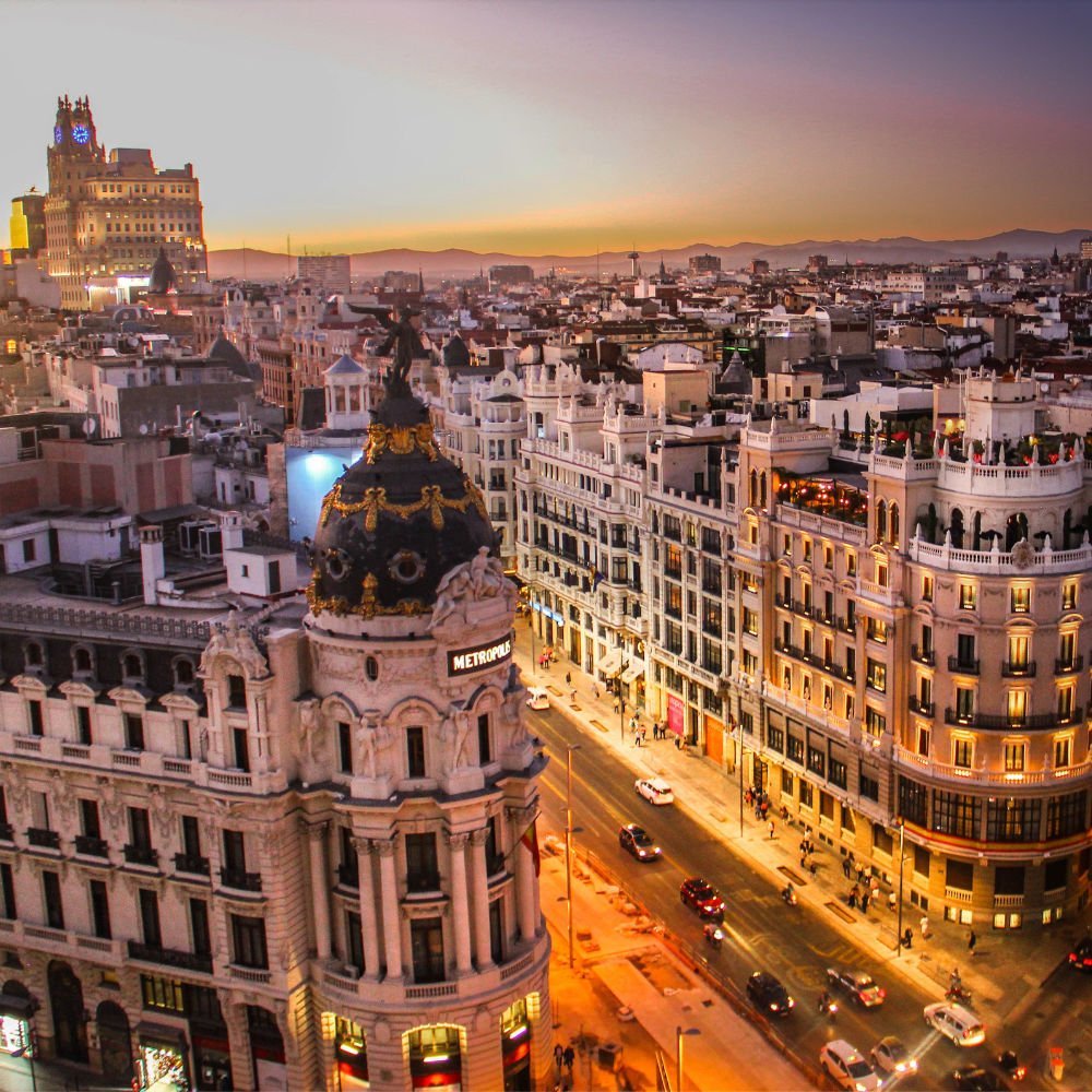 A city skyline of madrid at sunset. larg building loom below and the horizon is lined with faint mountains