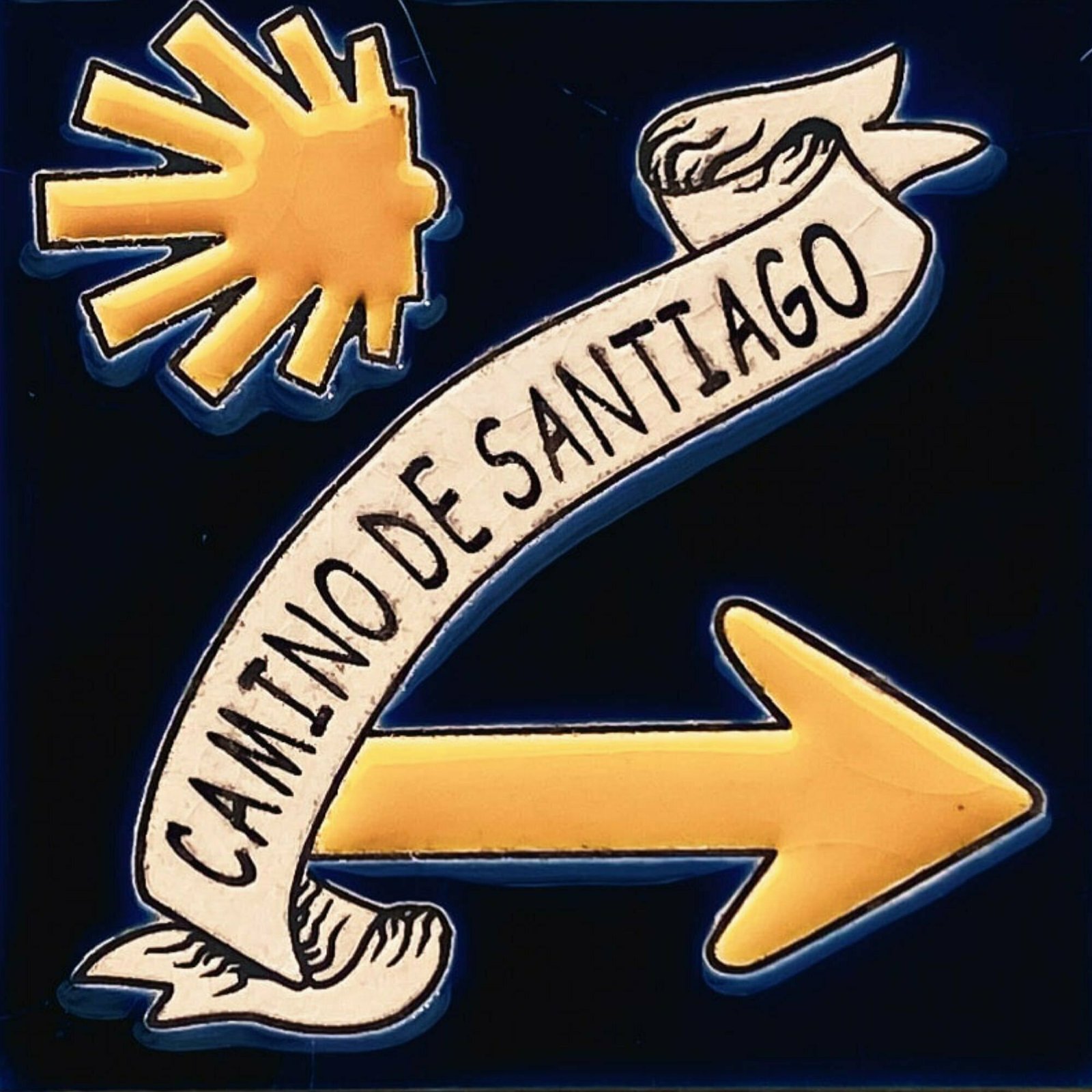 a sign for the camino de Santiago is embossed on a dark blue tile with a pastel orange shell logo and directional arrow pointing to the right
