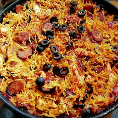 A large paella pan sits on a counter and is filled with chicken and chorizo pasta.