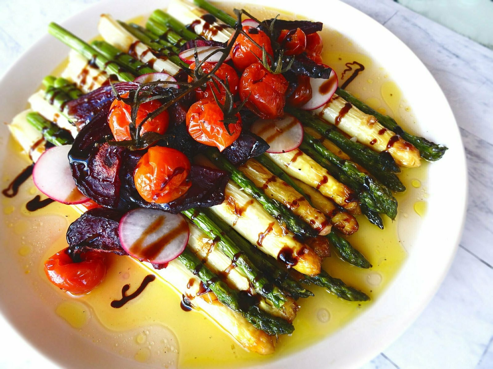 A large white plate sits loaded with a stack of roasted asparagus, and caramelized red onions.