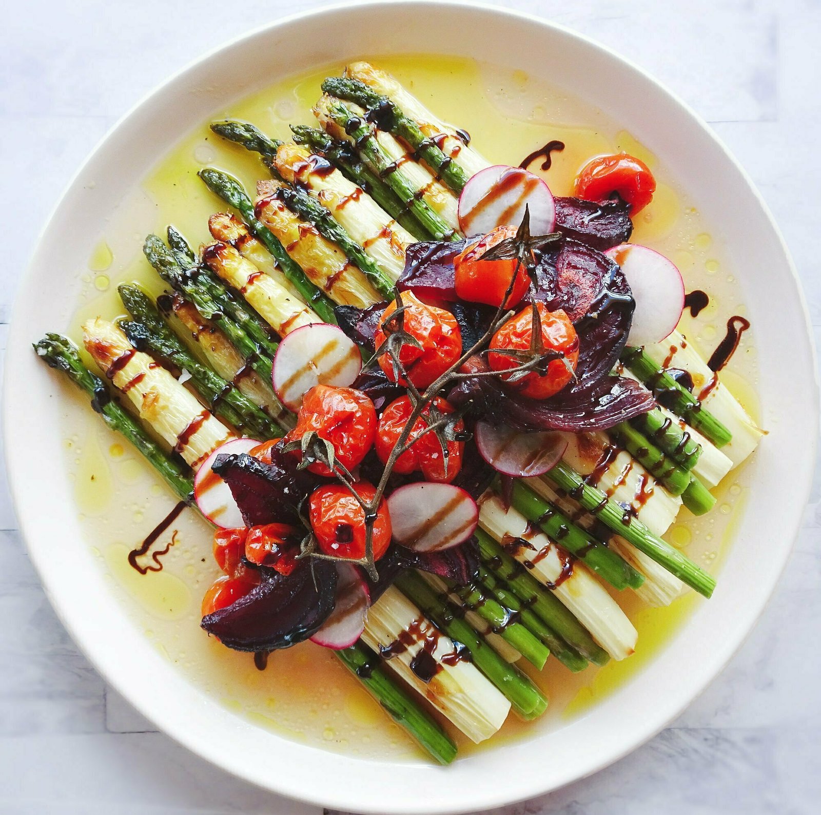 a large platter of roasted vegetables sits on a bed of roasted green and white asparagus