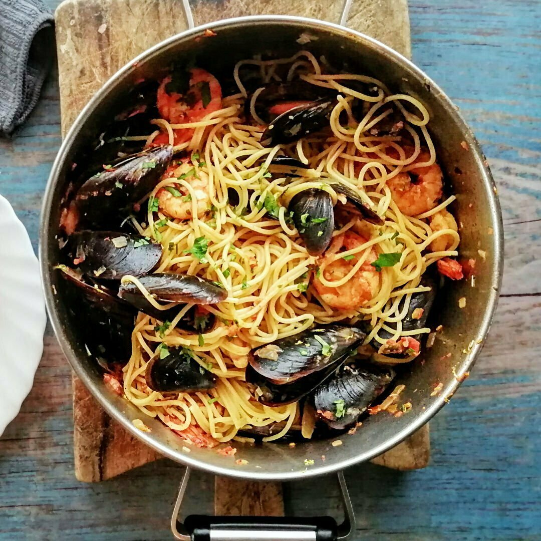 A large pot sits on a rustic blue background and is filled with shrimp and mussels pasta