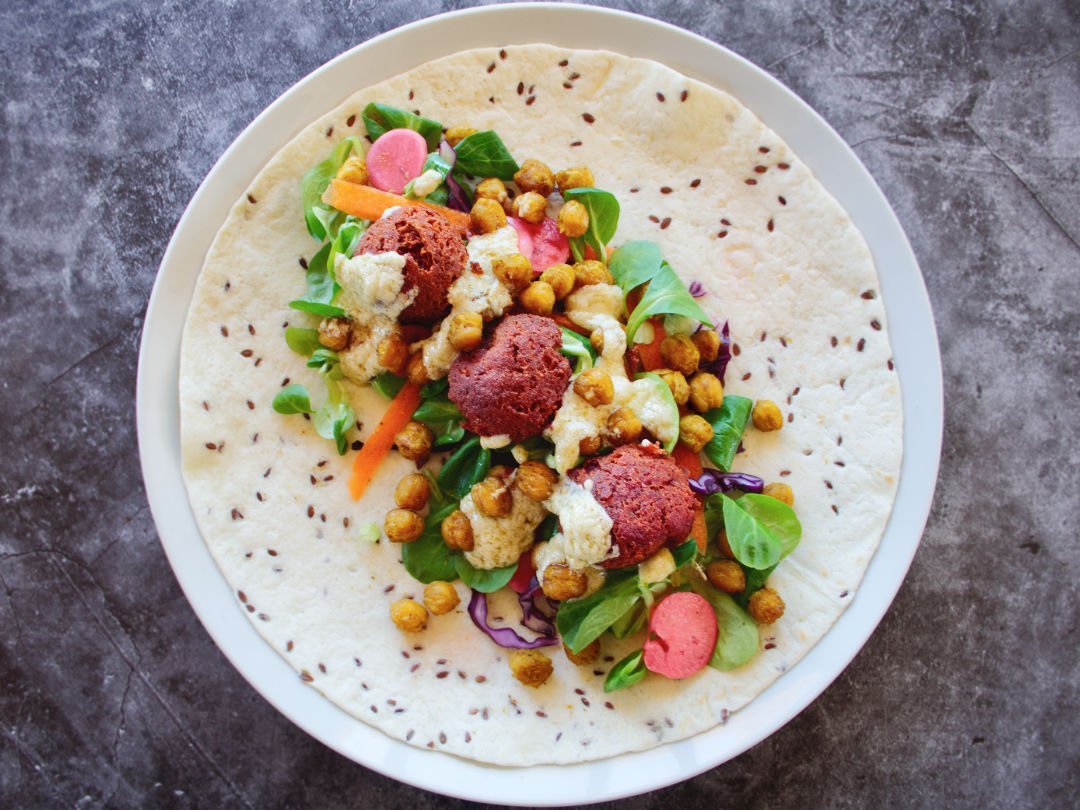 a wrap with salad and beetroot falafels sits on a white plate