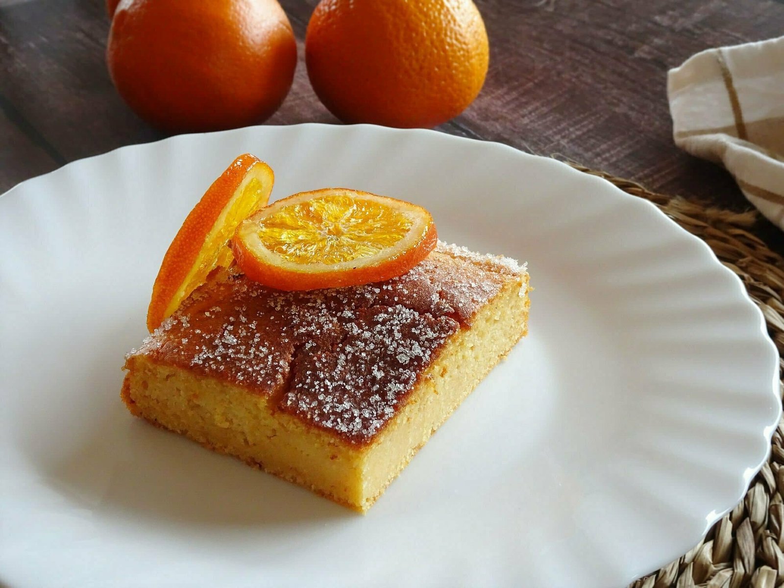 A slice of orange and grapefruit cake sits on a white plate and is garnished with a slice of candied orange