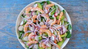 Shrimp avocado salad sits on a white plate with a rustic blue board background