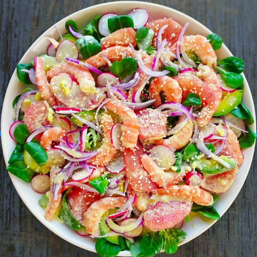 Around plate sit on a wooden counter full of color shrimp avocado salad