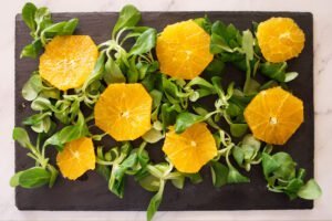 Greens and orange slices sit on a slate plate