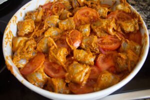 a large casserole dish with some fish fillets tomatoes red onion and romesco sauce mixed together