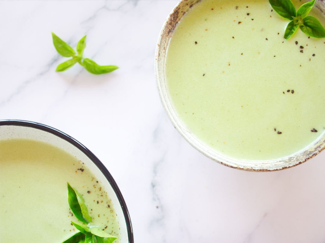 2 bowls sit filled with cold cucumber soup and garnished with some fresh basil