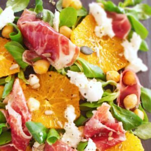 A large platter of jamon iberico sald sits topped with mozarella salad greens chickpeas and seasoned with salt and pepper