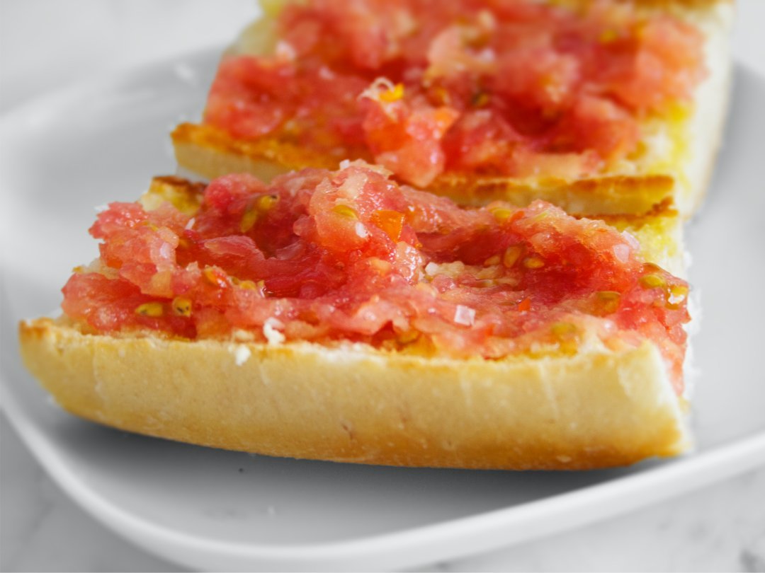 a white plate sits on a marble counter with two slices of pan con tomate