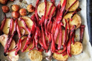 an oven tray filled with roasted pepper, scalloped potatoes, and cherry tomatoes