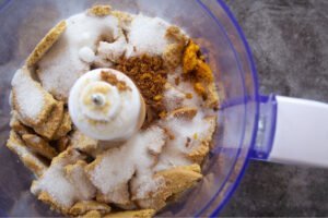 ingredients are added to a blender to make a biscuit base for a walnut caramel tart