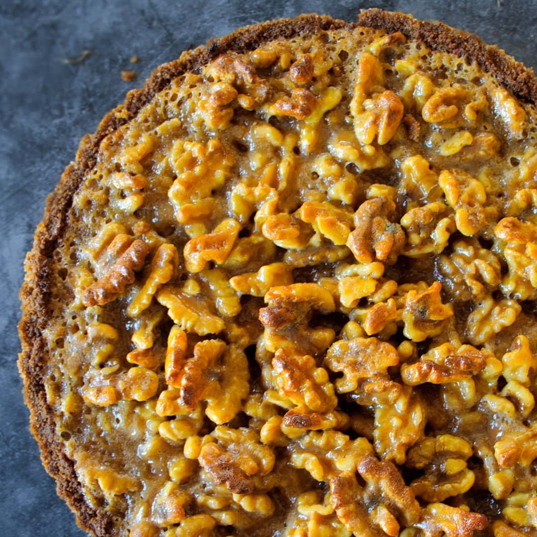 a golden walnut tart sits on a blue countertop.