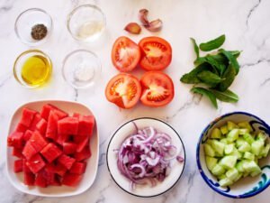 INgredients for watermelon gazpacho are laid out on a marble countertop
