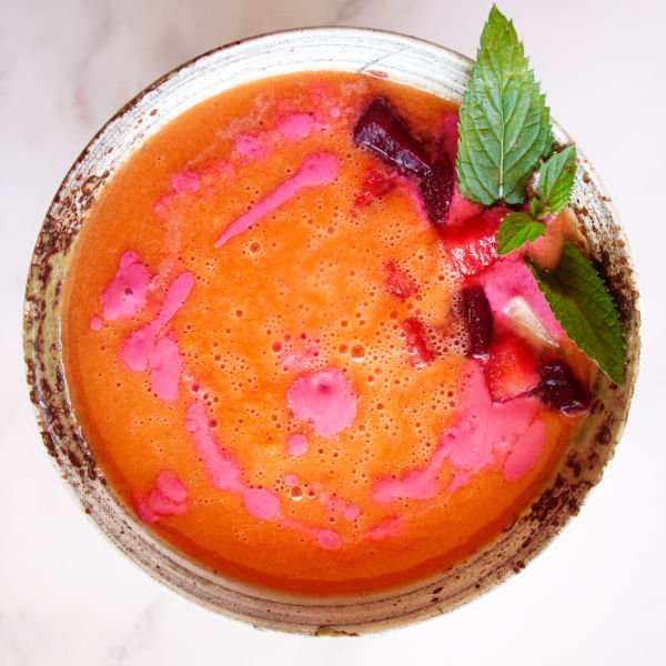 a ceramic bowl of watermelon gazpacho is garnished with some sprigs of fresh mint 