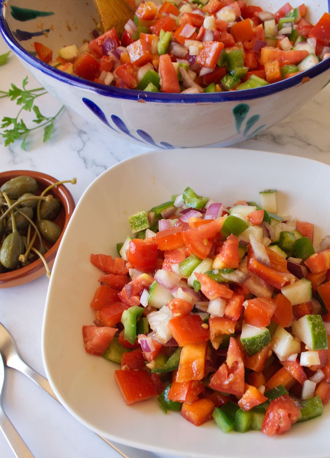 A large colorful bowl of Pipirrana Spanish Salad sits waiting to be served to a small white bowl
