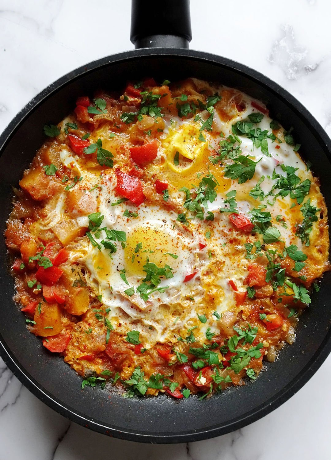 A large frying pan holds some pisto with eggs sprinkled with some fresh chopped parsley. 