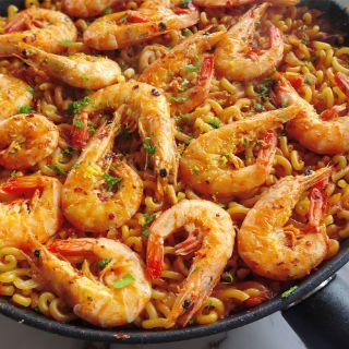 A large pan of fideua marisco sist on a counter decoratedw ith large cooked shrimp