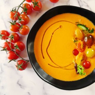 a large bowl of gazpacho andaluz sits beside some cherry tomatoes