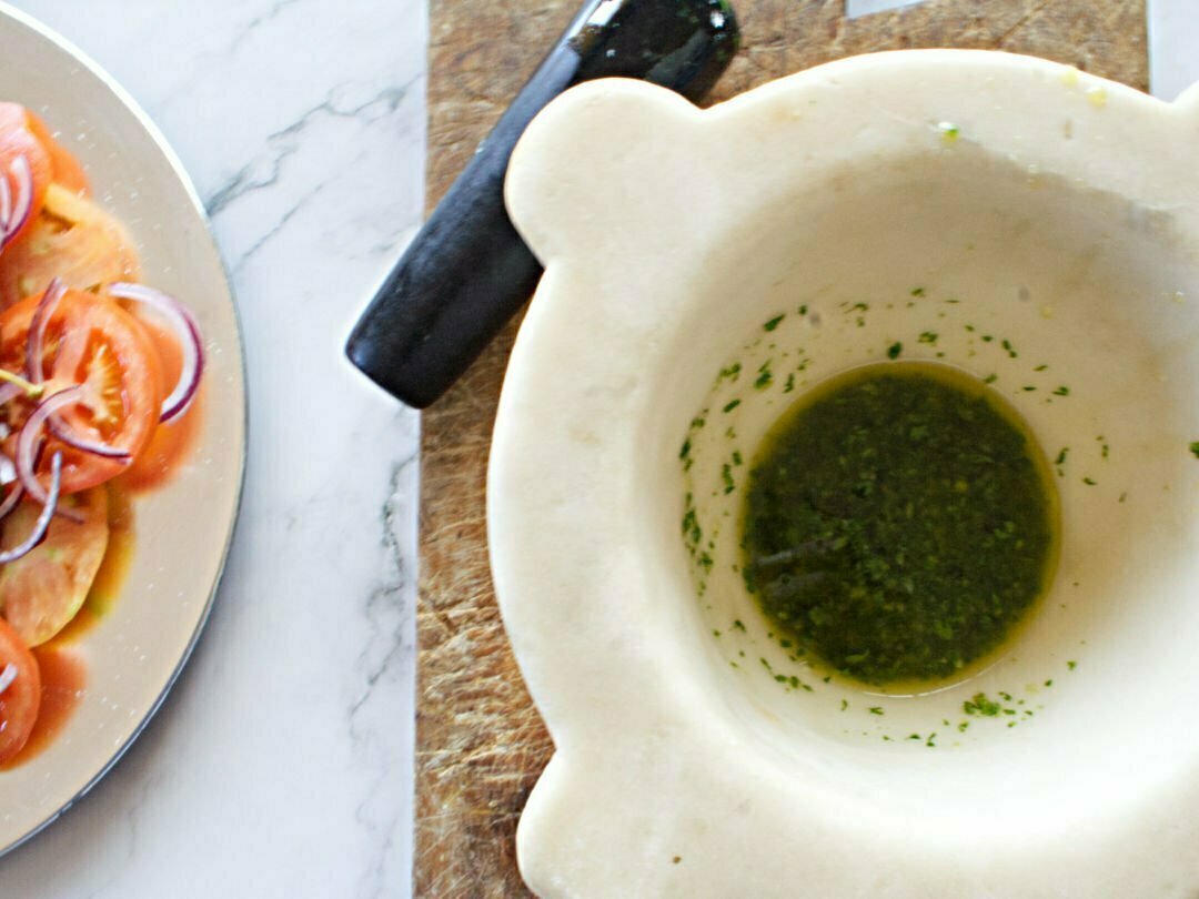 A large white marble mortar sits with some homemade green pesto in the bottom