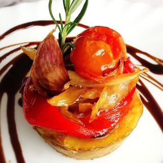 A small stack of roasted veggies sits garnished with some caramelized onion and a cherry tomato. 