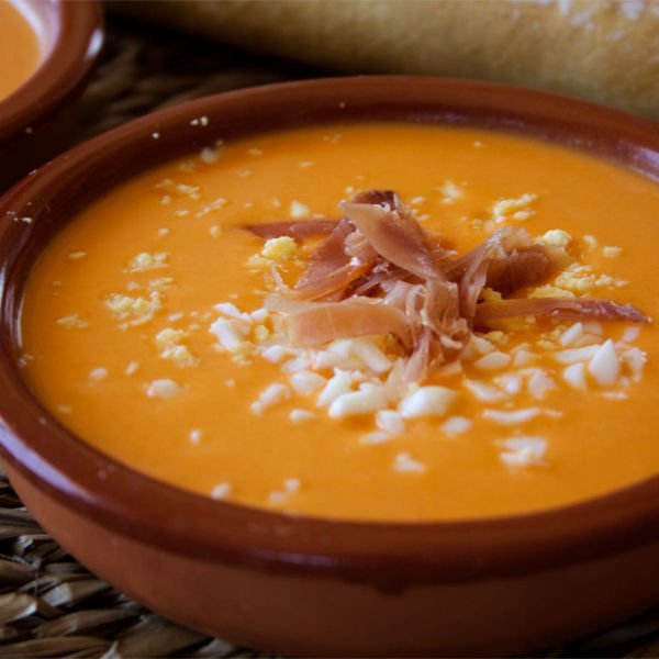 an earthenware dish holds a tapas serving of salmorejo with some serrano ham and egg garnishing