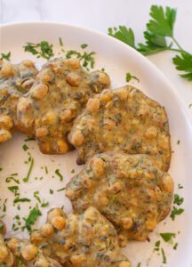 Oven baked chickpea fritters sit on a white plate with a sprinkling of chopped parsley