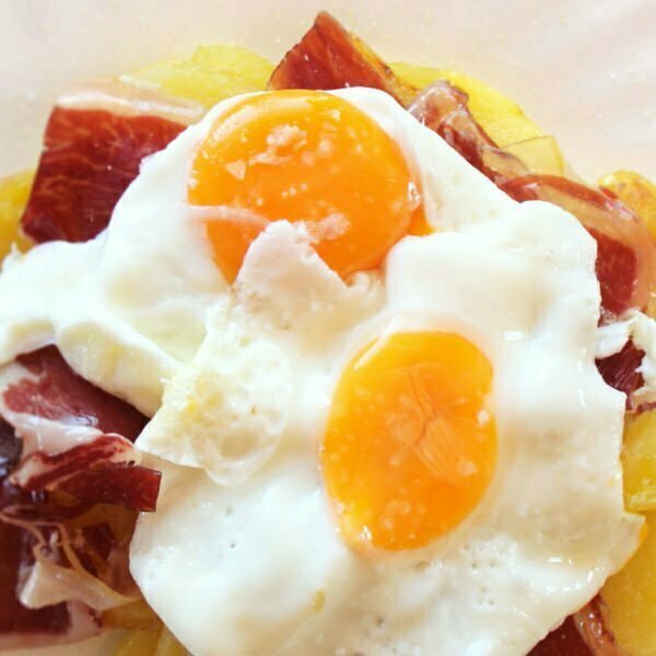 A plate of huevos estrellados sits with potatoes eggs and ham