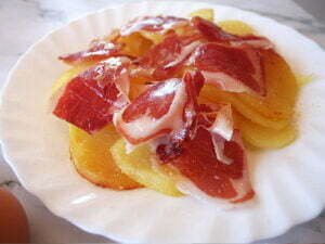 a plate of golden fried potatoes with some jamon iberico on top