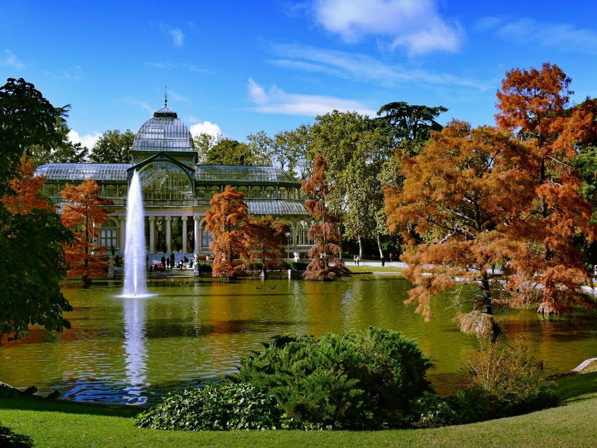 a view over a lake to a large glasshouse structure in retiro park