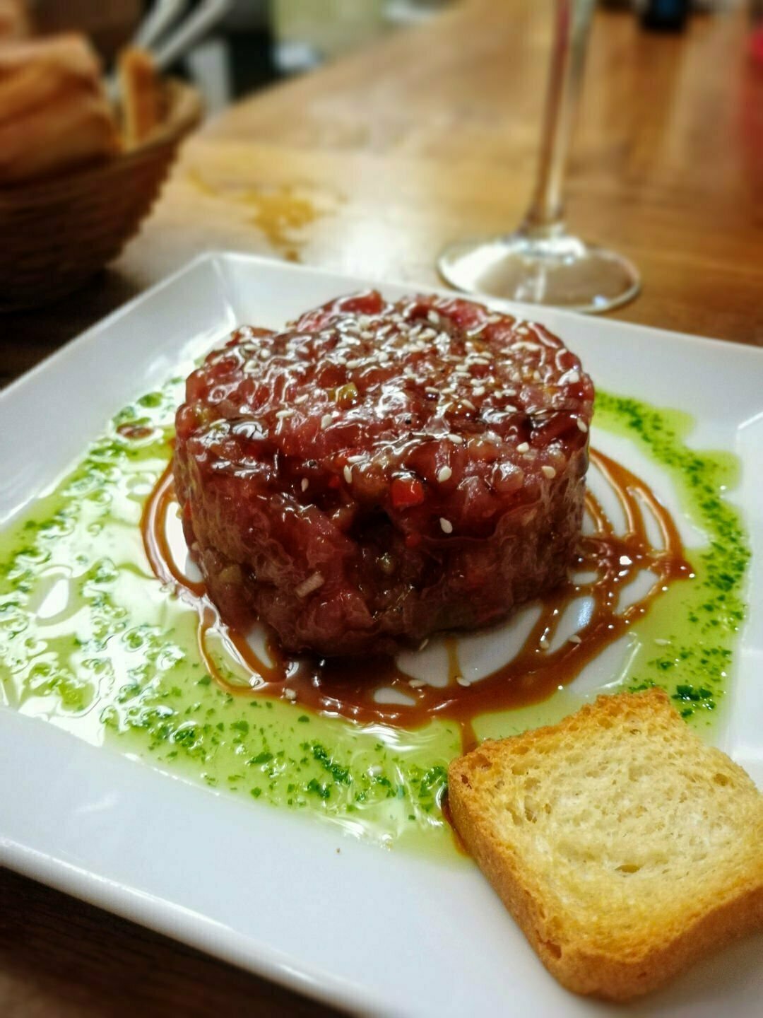 A plate of tuna tartare sits with some green parsley and oil garnish