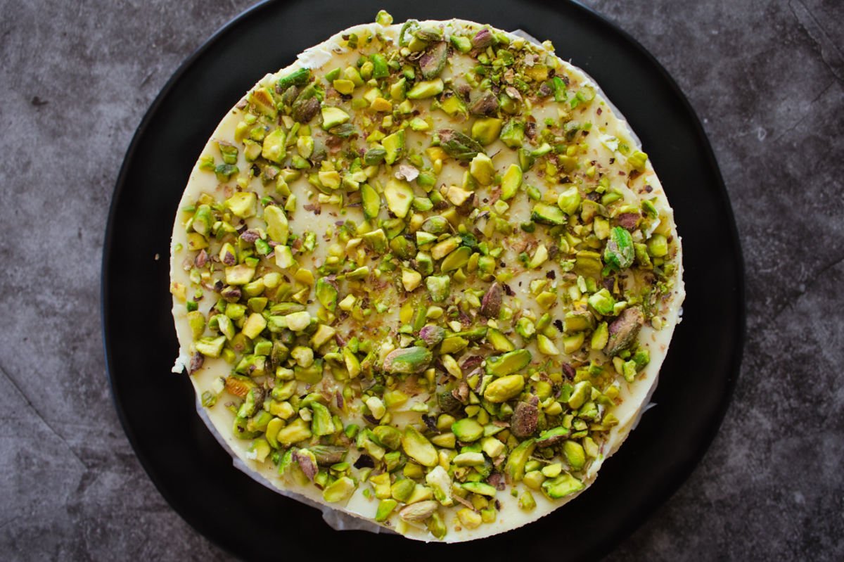 ariel view looking down on a circular white chocolate cheesecake with pistachio nut topping