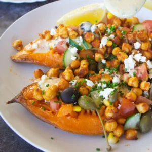 medibakedsweetpotatoesthumb600x The Spanish Radish a large baked sweet potato sits on a white plate with plenty of Mediterranean inspired toppings