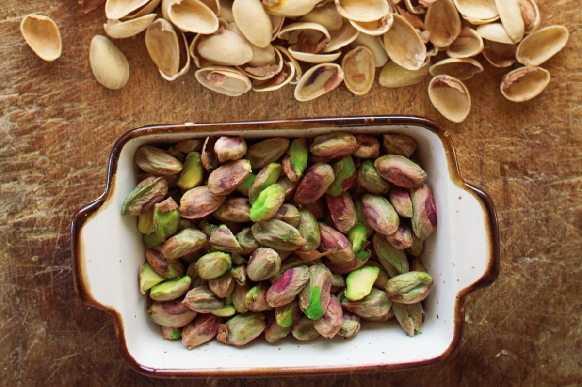 Some shelled pistachio nuts sit in a small bowl on a chopping board