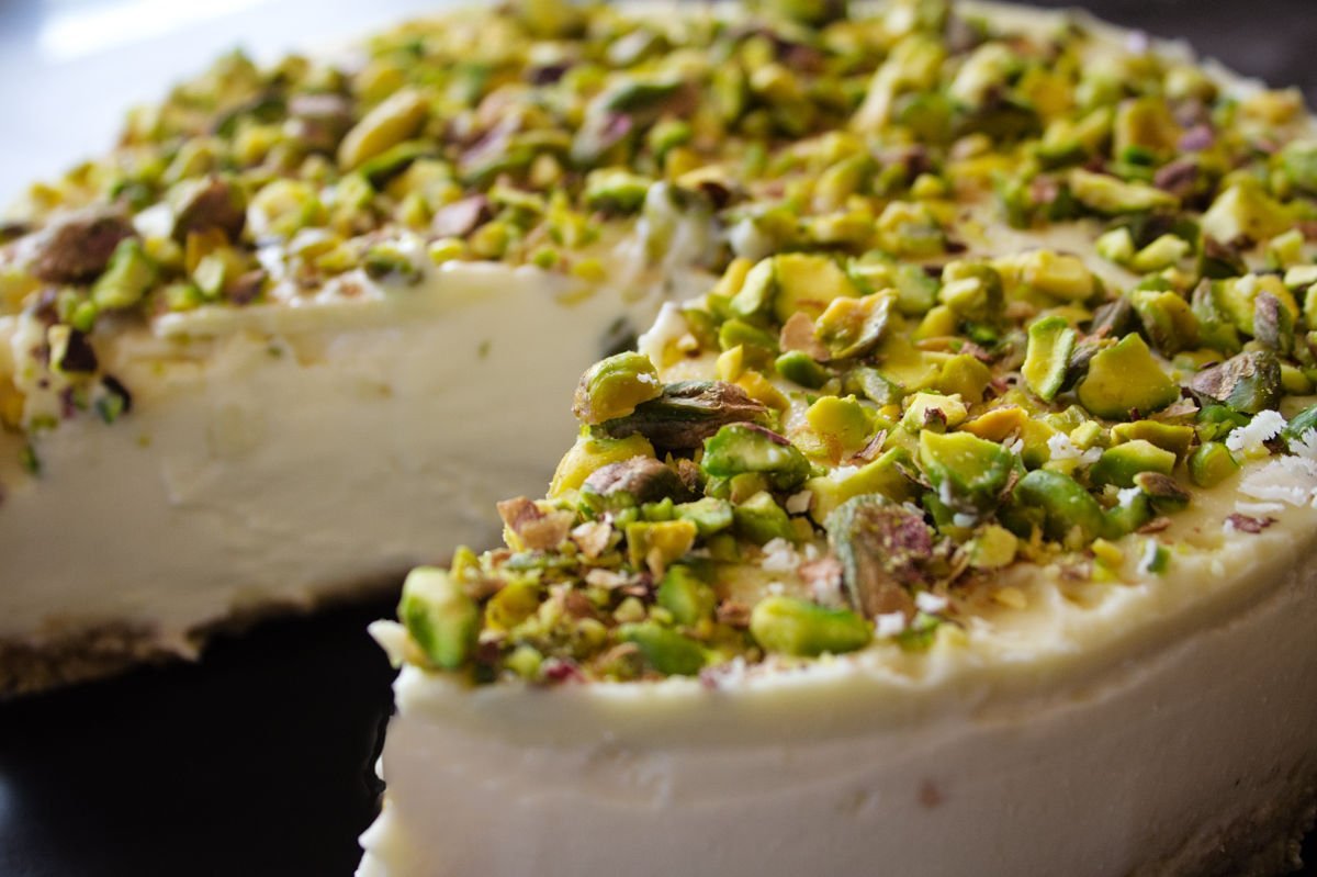 A white chocolate cheesecake with a green pistachio nut topping sits with a large slice removed
