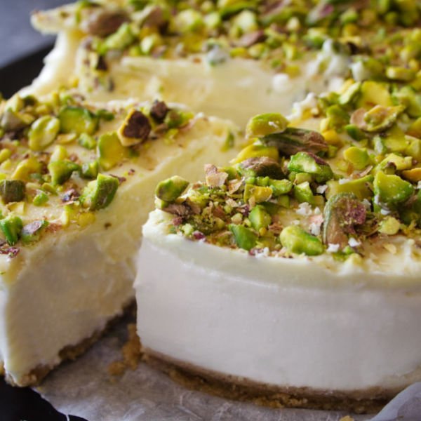 A white chocolate cheesecake is topped with lots of crushed pistachio nuts