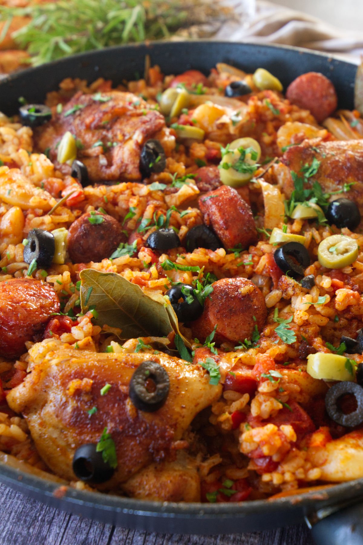 A pan of cooked chicken and chorizo rice, with olives and bay leaves on top.