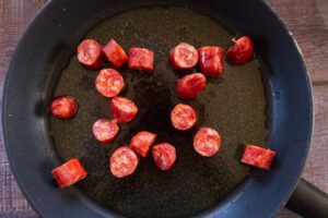 Some pieces of raw chorizo sit in a pan with some olive oil