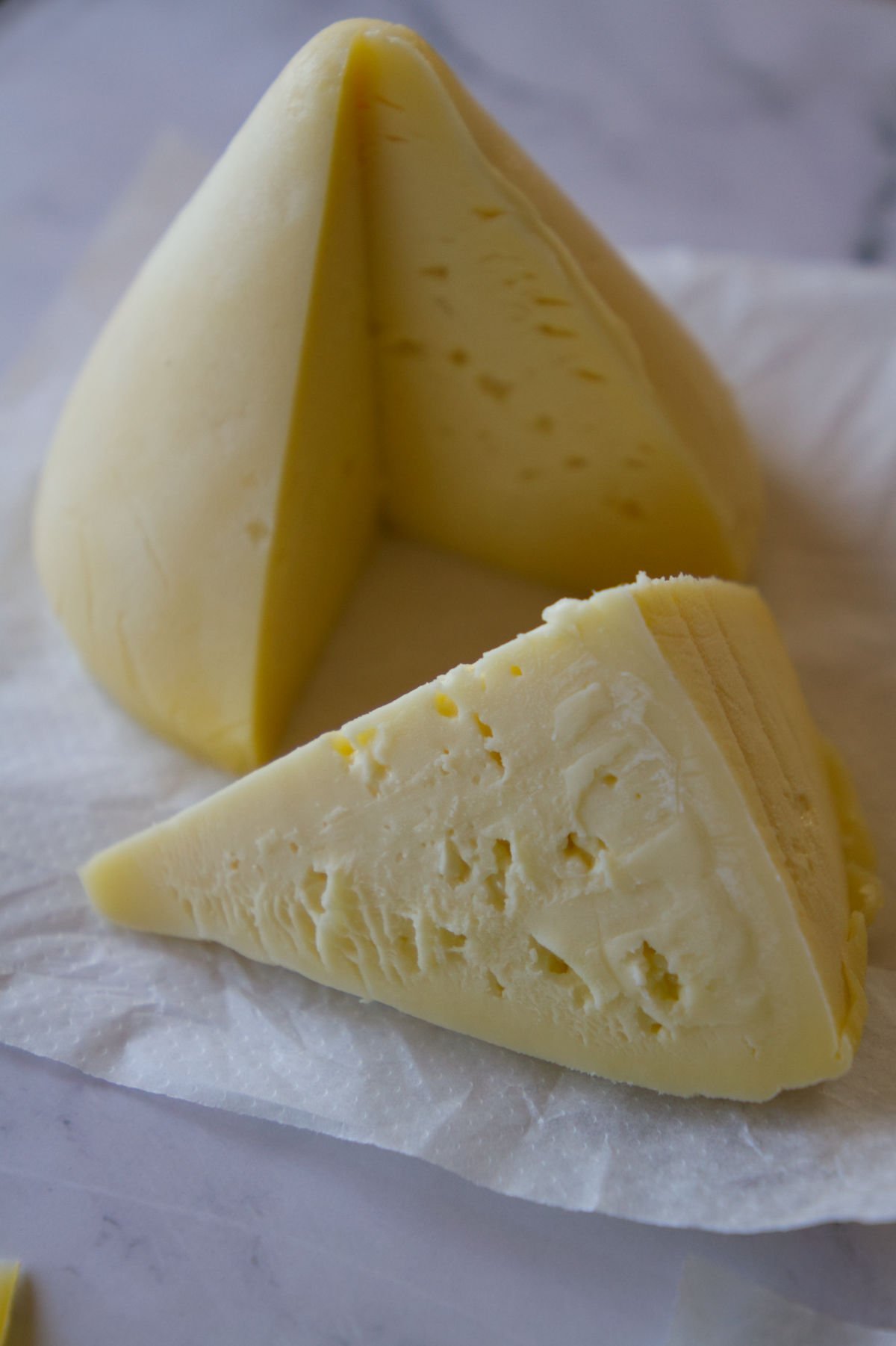 A large peice of tetilla cheese sits with a wedge cut.